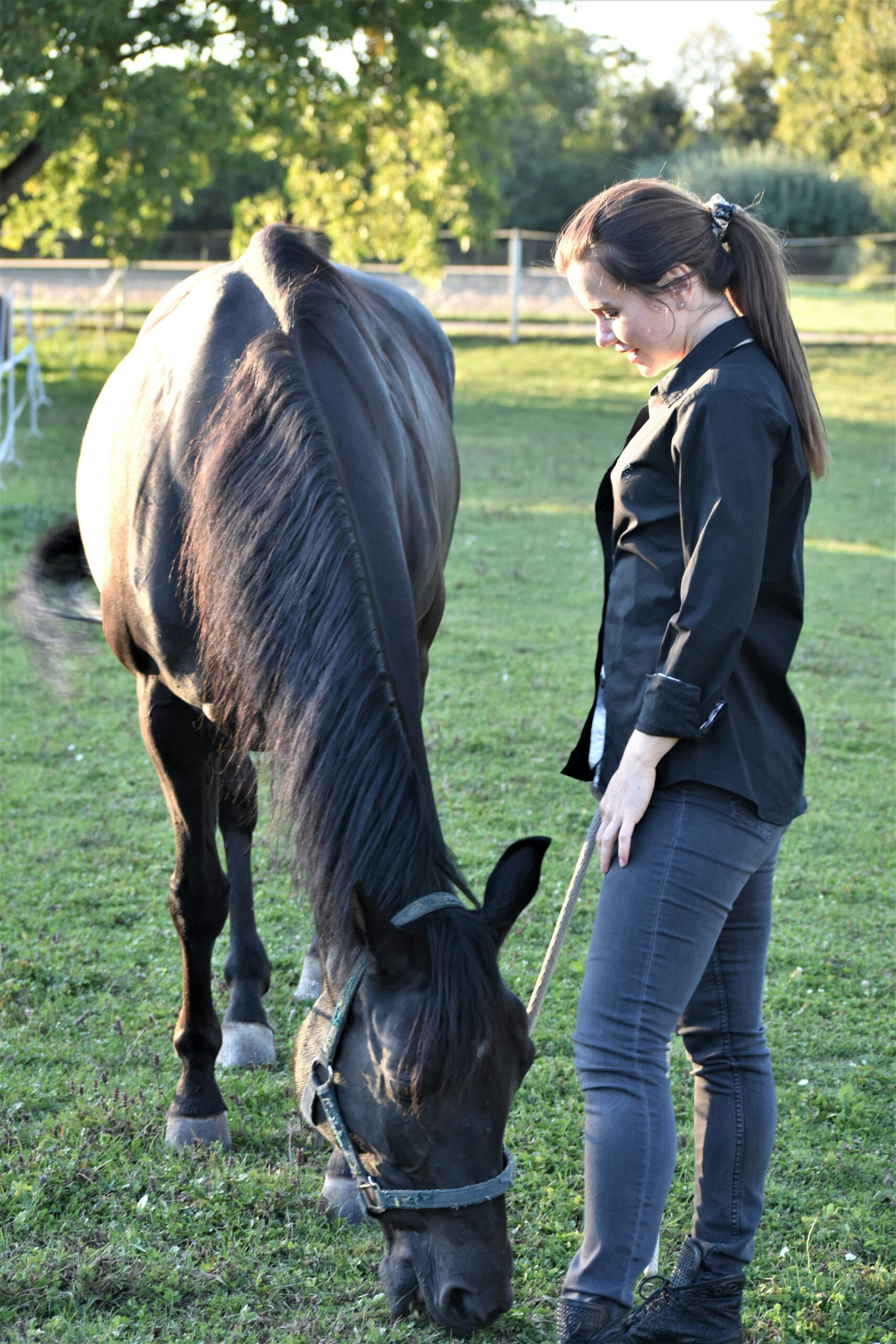 a woman standing next to a brown horse on a lush green field