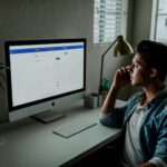 man in blue denim jacket facing turned on monitor